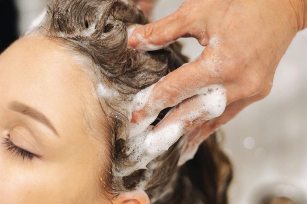 chica exfoliándole el cabello para eliminar la grasa del cuero cabelludo jpg